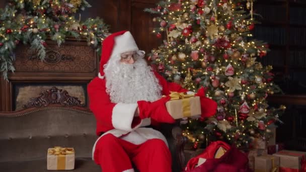 Noel Baba hediyelerini çantaya koyup Noel ağacı yakınındaki yeni yıl kutlamalarına hazırlanıyor. — Stok video