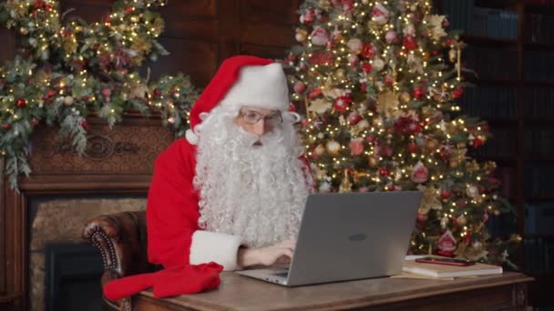 Retrato de Papai Noel pensativo digitando com laptop moderno em casa decorada — Vídeo de Stock