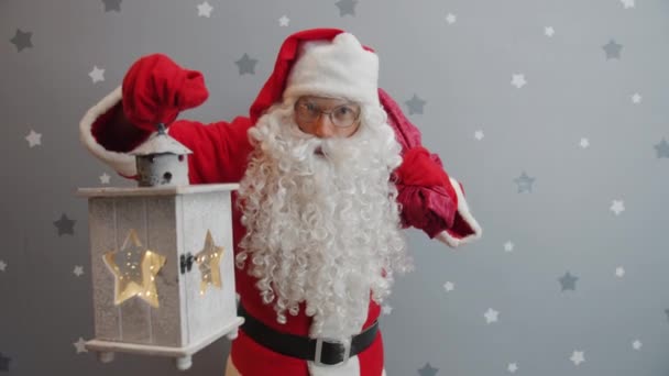 Santa Claus drží lucernu a tašku darů při pohledu na kameru na hvězdném pozadí — Stock video