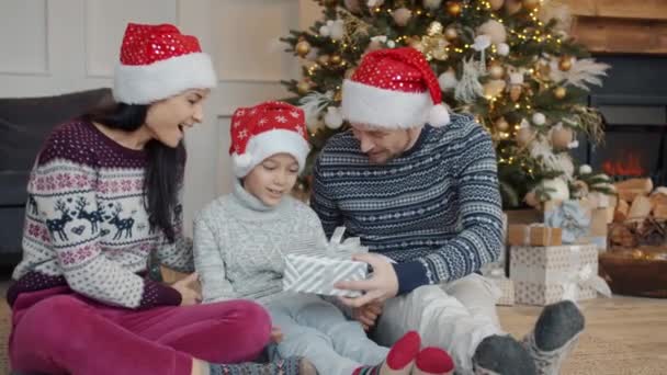 I genitori in cappelli di anno nuovo che danno il regalo a bambino felice la vigilia di Natale a casa — Video Stock