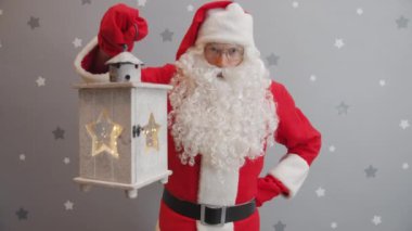 Noel Baba 'nın portresi fener kaldırıyor ve gri arka plandaki kameraya bakıyor.