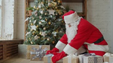Geleneksel kıyafetli Noel Baba tatilde Noel ağacının altına hediye koyar.