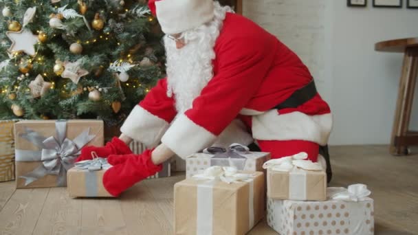 Noel Baba kostümlü bir adam yeni yıl ağacının altına hediyeler yerleştiriyor. — Stok video