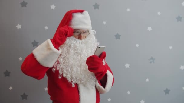 Santa Claus using smartphone touching screen standing on grey starry background — Stock Video