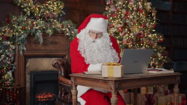 Człowiek w stroju Świętego Mikołaja pracuje z komputerem w pomieszczeniach w urządzonym domu — Wideo stockowe