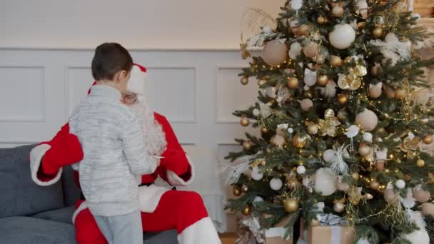 Cute little boy dając list do Świętego Mikołaja na wakacje w nowoczesnym mieszkaniu — Wideo stockowe