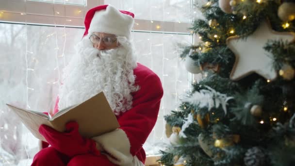 Zpomalení pohybu Santa Claus čtení knihy v blízkosti vánočního stromečku doma — Stock video