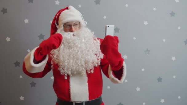 Noel Baba kostümüyle dans eden, kulaklık takan ve akıllı telefon kullanan adam. — Stok video