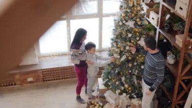 Erkek, kadın ve çocuk evdeki Noel ağacına güzel süslemeler yapıyor.