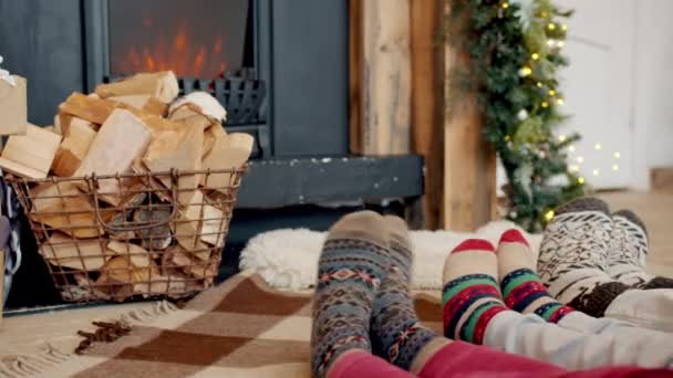 Κοντινό πλάνο μεγάλων και μικρών ποδιών σε χριστουγεννιάτικο στυλ κάλτσες που κινούνται με τζάκι στο φόντο — Αρχείο Βίντεο