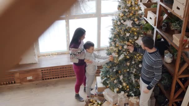 Man, kvinna och pojke sätta vackra dekorationer på julgran hemma — Stockvideo