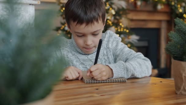 Portrét malého chlapce psaní dopis Santa Claus před Vánocemi ve zdobené místnosti — Stock video