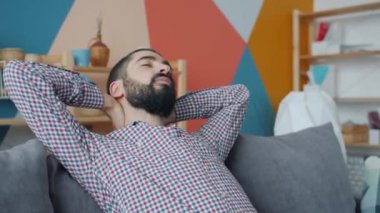 Orta Doğulu çekici bir adamın kanepede uzanmış boynunu gevşetiyor.