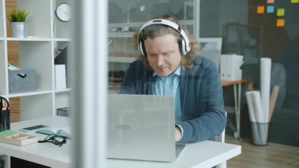 Zpomalení pohybu veselý zaměstnanec nosí sluchátka psaní s notebookem pak tanec baví — Stock video