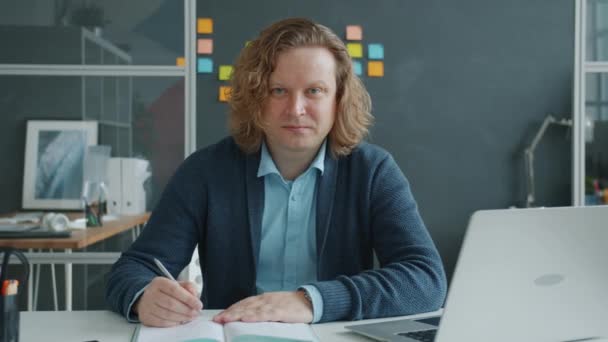 Portrait of attractive man looking at camera with serious face holding pen at desk in office — Stock Video