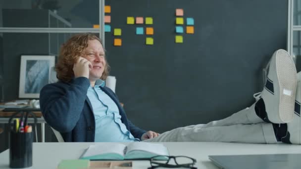 Cámara lenta de empresario alegre hablando por teléfono móvil y sonriendo en la oficina — Vídeos de Stock