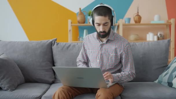 Aantrekkelijke Arabische man met behulp van laptop computer typen naar muziek luisteren via een hoofdtelefoon — Stockvideo