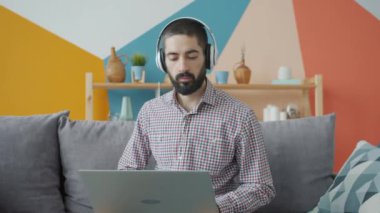Evde kulaklık takıp dizüstü bilgisayarla çalışan yakışıklı bir Arap.
