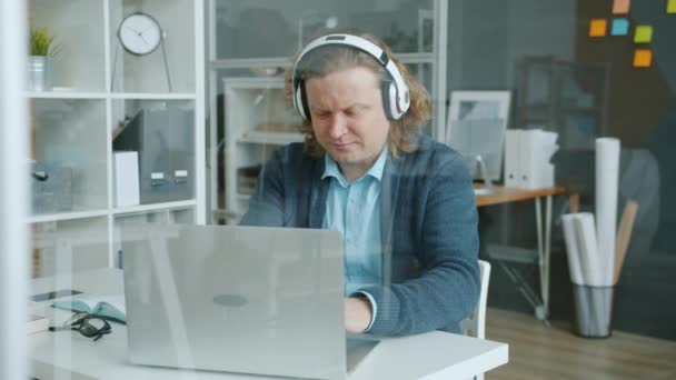 Trabalhador de escritório homem feliz digitando com laptop, em seguida, dançar se divertindo em fones de ouvido — Vídeo de Stock