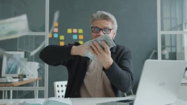 Zengin işadamı para saçıyor ve gülüyor modern ofiste başarının tadını çıkarıyor.