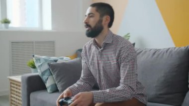 Kaygısız Orta Doğulu adam evde oyun oynarken joystick kullanıyor.