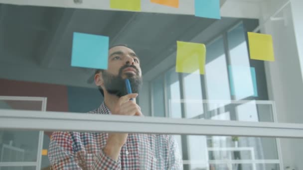 Porträt eines Mannes aus dem Nahen Osten, der im Büro klebrige Zettel an Glaswand klebt — Stockvideo