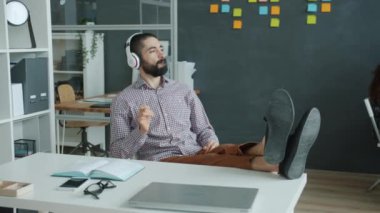 Arap adam modern ofiste eğleniyor müzik dinliyor gitar çalıyormuş gibi yapıyor kulaklık takıyor.