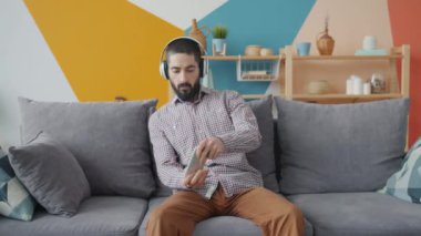 Arap adam apartmanda kablosuz kulaklık takarak mobil video oyunlarını seviyor.
