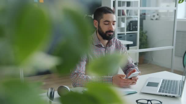 Χαρούμενος Άραβας που χρησιμοποιεί οθόνη αφής smartphone στο χώρο εργασίας απολαμβάνοντας τα μέσα κοινωνικής δικτύωσης στην εργασία — Αρχείο Βίντεο