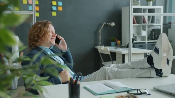 Радісний хлопець офіс працівник говорить на мобільному телефоні сміється і жестикулює на робочому місці — стокове відео