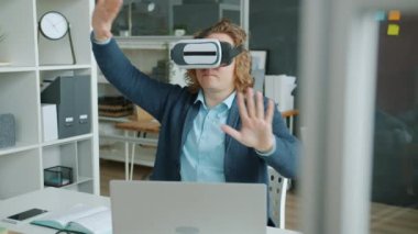 Sanal gerçeklik gözlüğü takan bir adamın ofiste kollarını hareket ettirmesi.