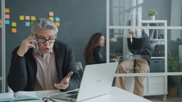 Verrückter Büroangestellter brüllt im Handy über Geschäftskonflikte und schlägt dann auf Schreibtisch ein — Stockvideo