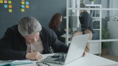Yorgun bir ofis çalışanı masa başında uyuyor sonra uyanıyor ve dizüstü bilgisayarla çalışıyor.