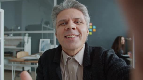 Portret van gelukkig volwassen man op zoek naar camera spreken zwaaiende hand het maken van video gesprek van kantoor — Stockvideo