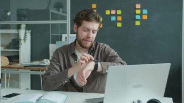 Genç işadamı dijital saat ekranına dokunuyor ve gülümsüyor.