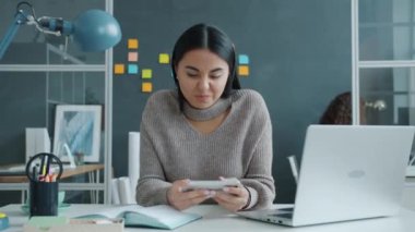 Ofiste akıllı telefondan dokunarak video oyunu oynayan mutlu yarış kızı.