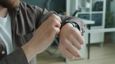 Erkek eli, akıllı saat ekranını araklıyor. Adam ofiste cihaz kullanıyor.