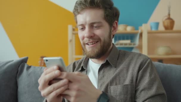 Slow motion van knappe man met behulp van smartphone sms 'en in modern appartement — Stockvideo