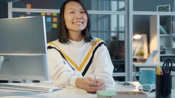 Portret van vrolijke Aziatische werknemer glimlachend aan de computer bureau in het kantoor — Stockvideo