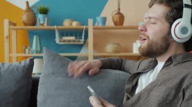 Kulaklık takıp müzik dinleyen genç adam evde akıllı telefon tutuyor.