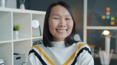 Modern ofiste gülümseyen mutlu Asyalı kızın portresi. Meslektaşı arka planda çalışıyor.