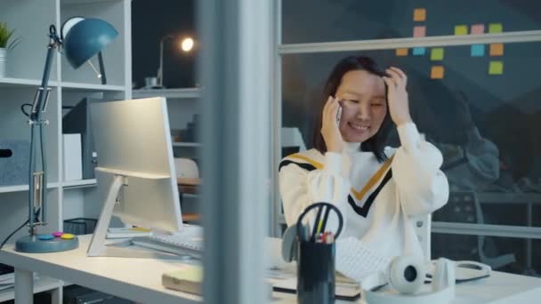 Radostné asijské žena kancelář pracovník chatování na mobilním telefonu v moderní kanceláři v noci — Stock video