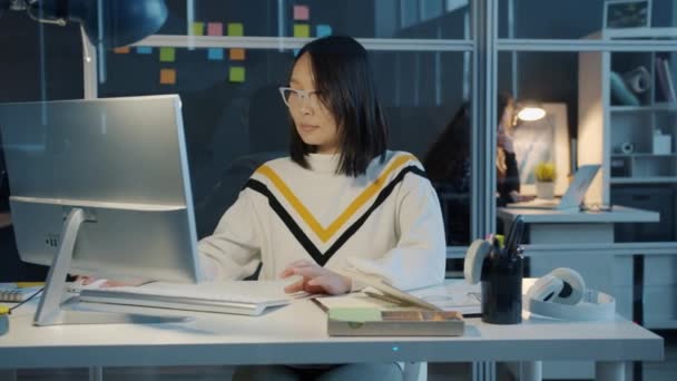 Portret van Aziatische zakenvrouw met behulp van computer en het nemen van notities in notebook in het kantoor in de avond — Stockvideo