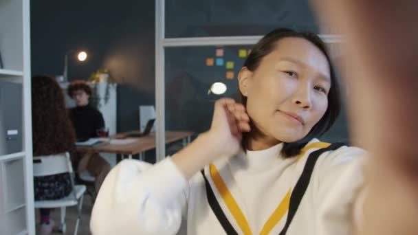 Portret szczęśliwej Azjatki robiącej selfie w ciemnym biurze patrzącej na aparat i pozującej gestami dłoni — Wideo stockowe