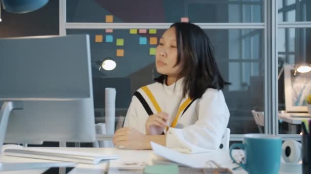 Unavená asijské dívka spí v tmavé kanceláři pak se probudí a pracuje s počítačem — Stock video