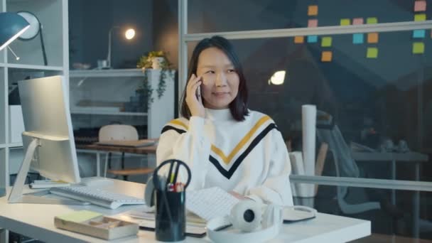 Portret van Aziatische vrouw spreken op mobiele telefoon en gebaren in donkere werkplek — Stockvideo