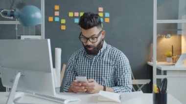 Mutlu Orta Doğulu adam akıllı telefon mesajlarını kontrol ediyor. Ofiste iyi haberlerin tadını çıkarıyor.