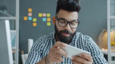 Mutlu Orta Doğulu işadamı ofiste akıllı telefondan video oyunu oynayarak eğleniyor.