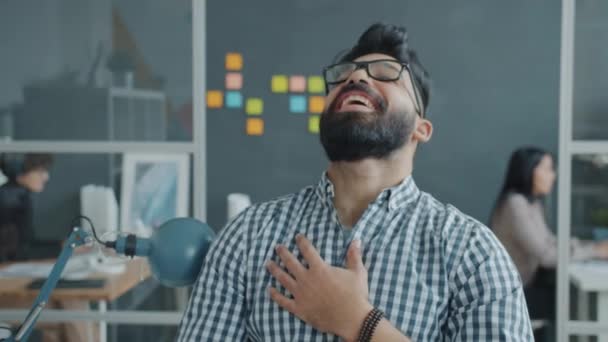 Retrato de alegre hombre de Oriente Medio riendo en la oficina, las mujeres están trabajando en segundo plano — Vídeos de Stock