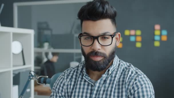 Retrato de homem de raça mista atraente usando óculos sorrindo no local de trabalho moderno — Vídeo de Stock